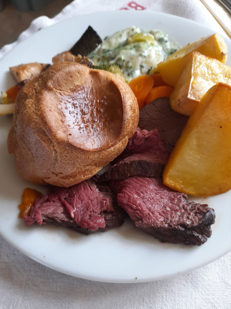 roast beef, yorkshire oudding and roast potatoes on a white circular plate